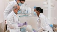 professor teaching two dental students over clinical dummy
